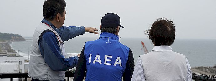 IAEA-Generaldirektor und noch zwei Personen stehen auf einem Dach des Atomkraftwerkes Fukushima Daiichi und blicken auf den Ozean.